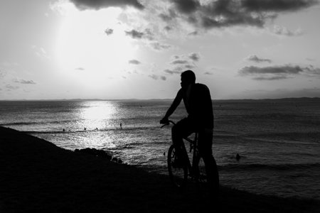 Salvador, Bahia, Brazil - October 01, 2021: Silhouette of a man on a bicycle enjoying the sunset against the sea in Salvador, Bahia, Brazil.のeditorial素材