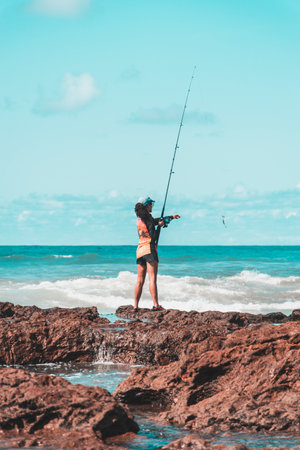 Salvador, Bahia, Brazil - October 10, 2021: Fisherman woman with fishing rod on the rocks fishing on the famous Rio Vermelho beach in Salvador, capital of Bahia, Brazilのeditorial素材