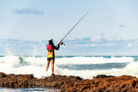 Salvador, Bahia, Brazil - October 10, 2021: Fisherman woman with fishing rod on the rocks fishing on the famous Rio Vermelho beach in Salvador, capital of Bahia, Brazilのeditorial素材