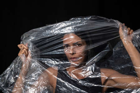 Model portrait with clear plastic in front of her face against black background. Salvador, Bahia,...