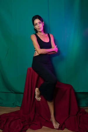 Portrait of adult model sitting on wooden chair against dark green background. Salvador, Bahia, Brazil.の写真素材