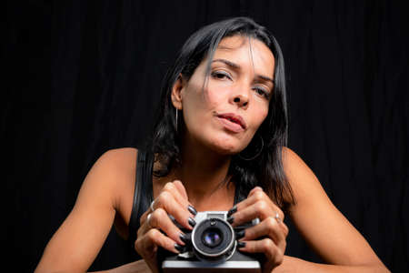 Portrait of a woman with photo camera against black background. Salvador, Bahia, Brazil.の写真素材