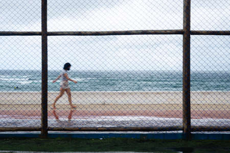 Silhouettes of people passing behind the sports fence during the rain. Salvador, Bahia, Brazil.の写真素材