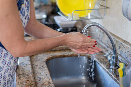 Young woman washing her hands at the kitchen sink.の写真素材