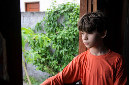 Portrait of a boy at the window wearing orange shirt. Salvador, Bahia, Brazil.の写真素材