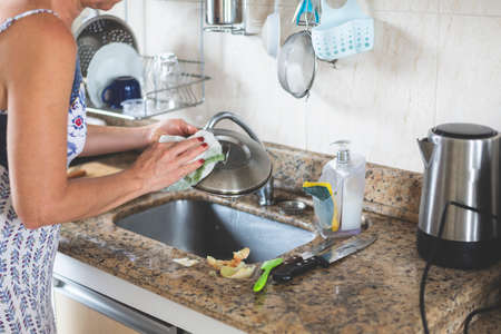 Young woman washing stainless steel pan in the kitchen sink.の写真素材