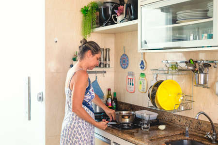 Young woman making food in pan with green plastic spatula.の写真素材