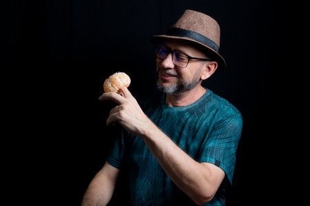 Man in glasses hat and beard holding a tangerine against black background. Salvador, Bahia, Brazil.の写真素材