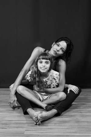 Black and white portrait of mother and daughter sitting on wooden floor. Salvador, Bahia, Brazil.の写真素材