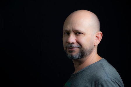 Portrait of a bald bearded man looking at the camera against a black background. Salvador, Bahia,...