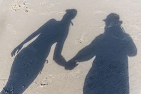 The top down view of a familys shadows on the beach sand. A man in a hat is holding hands with a woman in a bikini and cap. Praia do Guaibim, coast of the sea of Bahia, Brazilの写真素材