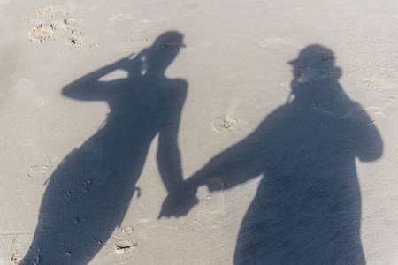 The top down view of a familys shadows on the beach sand. A man in a hat is holding hands with a woman in a bikini and cap. Praia do Guaibim, coast of the sea of Bahia, Brazilの写真素材