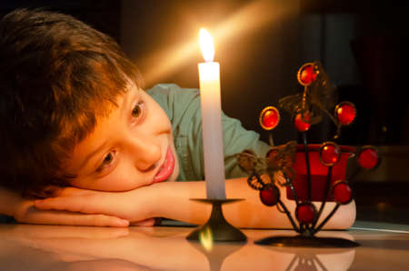 Child looking at a lit candle lying on the floor of the house. Salvador, Bahia, Brazil.の写真素材