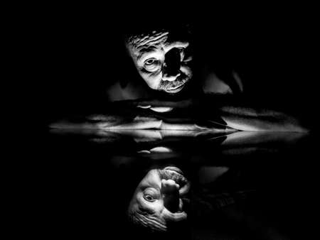 Black and white closeup of man face lying on glass with reflection. Salvador, Bahia, Brazil.