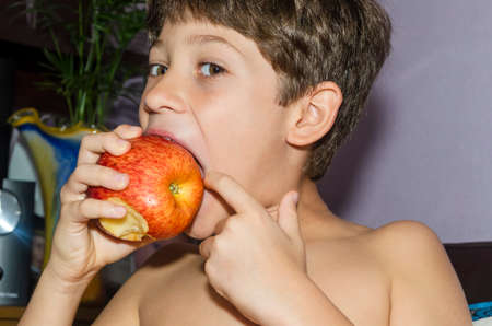 Child eating red apple at home. Salvador, Bahia, Brazil.の写真素材