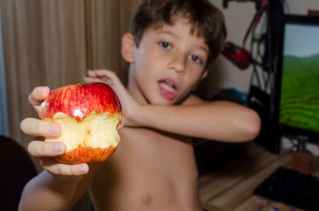 Child eating red apple at home. Salvador, Bahia, Brazil.の写真素材