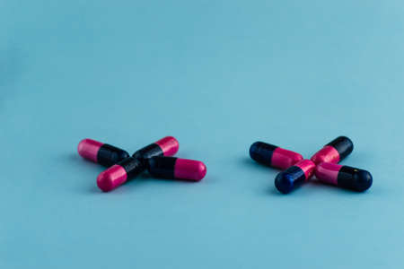 Simple pile of pink and black pills. Medicines, pills stacked on blue background. Medical supplies.の写真素材