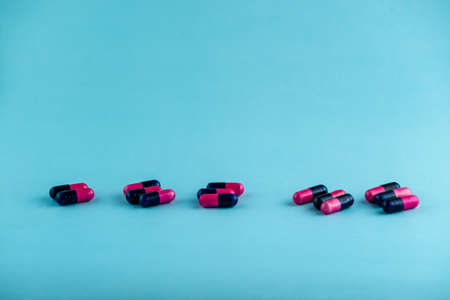 Simple pile of pink and black pills. Medicines, pills stacked on blue background. Medical supplies.の写真素材