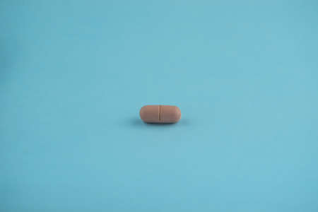 One brown colored pill on light blue surface. Medical supplies.の写真素材