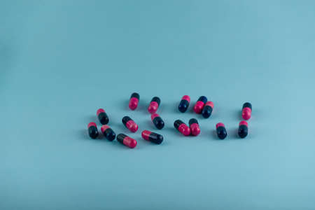 Simple pile of pink and black pills. Medicines, pills stacked on blue background. Medical supplies.の写真素材