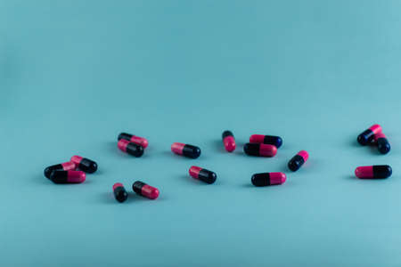 Simple pile of pink and black pills. Medicines, pills stacked on blue background. Medical supplies.の写真素材