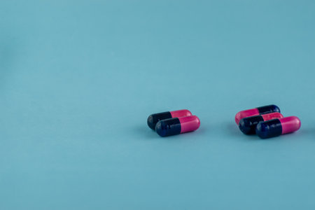 Simple pile of pink and black pills. Medicines, pills stacked on blue background. Medical supplies.のeditorial素材