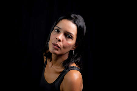 Studio portrait of young woman looking at camera against simple studio black background. She wears a black t-shirt.の写真素材