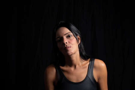 Studio portrait of young woman looking at camera against simple studio black background. She wears a black t-shirt.の写真素材
