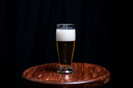 Studio Portrait of a glass cup with yellow liquid, on top of a wooden bench, against a black studio background. Salvador, Brazil.の写真素材