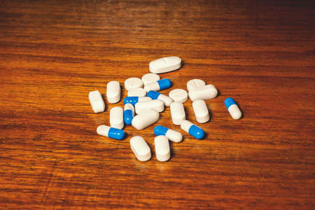 Simple pile of white and blue pills, medicines, pills stacked on brown background. Medical supplies.
