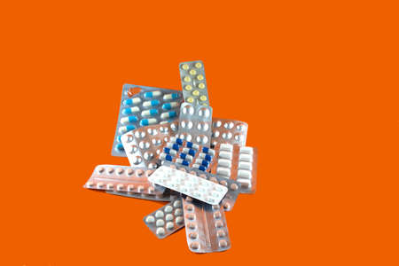 Carton of different pills, medicines, pills stacked on orange background. Medical supplies.