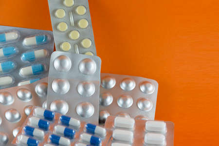 Carton of different pills, medicines, pills stacked on orange background. Medical supplies.