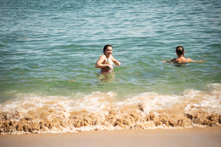 Mother and daughter in bikini entering the water at Porto da Barra beach in Salvador, Bahia.の写真素材