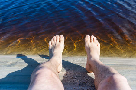 Legs of a man by the river against reddish water in the background. Guaibim beach in the city of Valenca, Bahia, Brazil.の写真素材