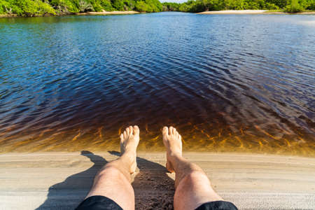 Legs of a man by the river against reddish water in the background. Guaibim beach in the city of...