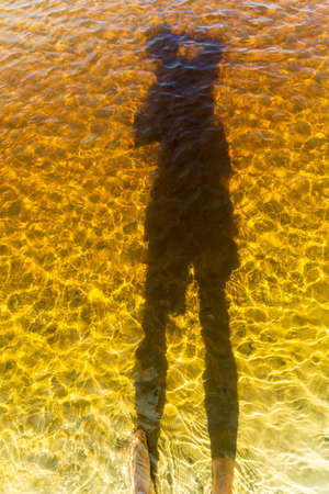 Shadow of a man wearing a hat, in the water of the Guaibimzinho River. Praia do Guaibim, coast of...