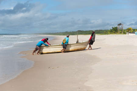 Fishermen are seen pushing a boat on the beach. Guaibim beach in the city of Valenca, Bahia, Brazil.の写真素材