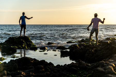 Salvador, Bahia, Brazil - December 11, 2021: Two fishermen fishing from above the rocks of Rio Vermelho beach in Salvador, Bahia.のeditorial素材