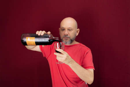 Young handsome man with beard, bald, red shirt wearing glasses holding in his hands a bottle of...