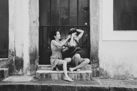 Black and white portrait of two beautiful and happy girls sitting against a green colored door. City girls far from the capital. They handle a carnival mask.の写真素材