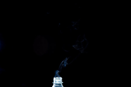 Smoke coming out of a plastic bottle against a black background. Background for Halloween. Texture...