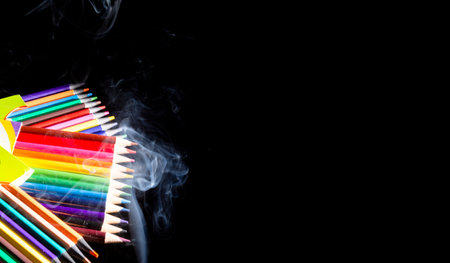 Colored pencils grouped on black background with white smoke coming from below. Closeup. Sharp pencil scraps.の写真素材