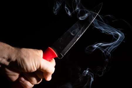 A sharp silver knife against a black background and smoke coming from below. Closeup.