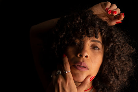Close-up portrait of a woman with her hands on her face and head against black background. Joy...