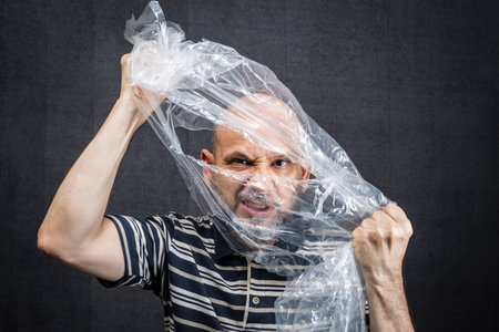 Mature man with a transparent plastic bag flying over his head and face. suffocate. face in a...