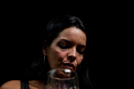 Portrait of young woman in black t-shirt drinking beer from glass cup. against black studio background. Salvador, Brazil.の写真素材