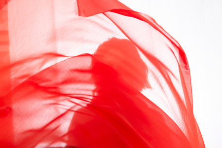 Young man with red transparent fabric in motion against white background. Studio photography.の写真素材