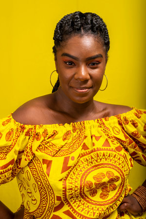 Close-up portrait of young, serious, beautiful woman, looking at camera, wearing colorful clothes. Isolated against yellow background.の写真素材