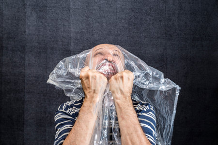 Mature man with a transparent plastic bag flying over his head and face. suffocate. face in a plastic bag, strangulationの写真素材
