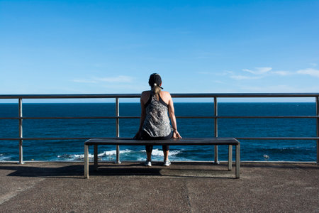 Beautiful woman sitting on wooden bench enjoying the beautiful sea. Beautiful day. back viewの写真素材